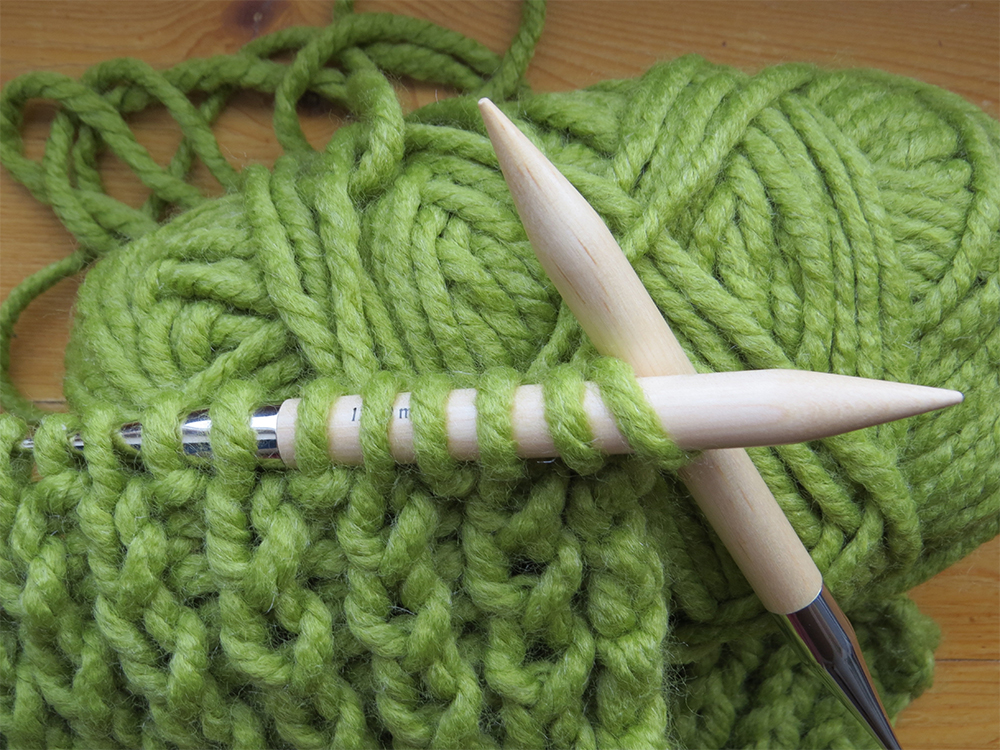 Gros plan sur une pelote de laine verte avec des aiguilles à tricoter en bois et quelques rangs de tricot en cours.