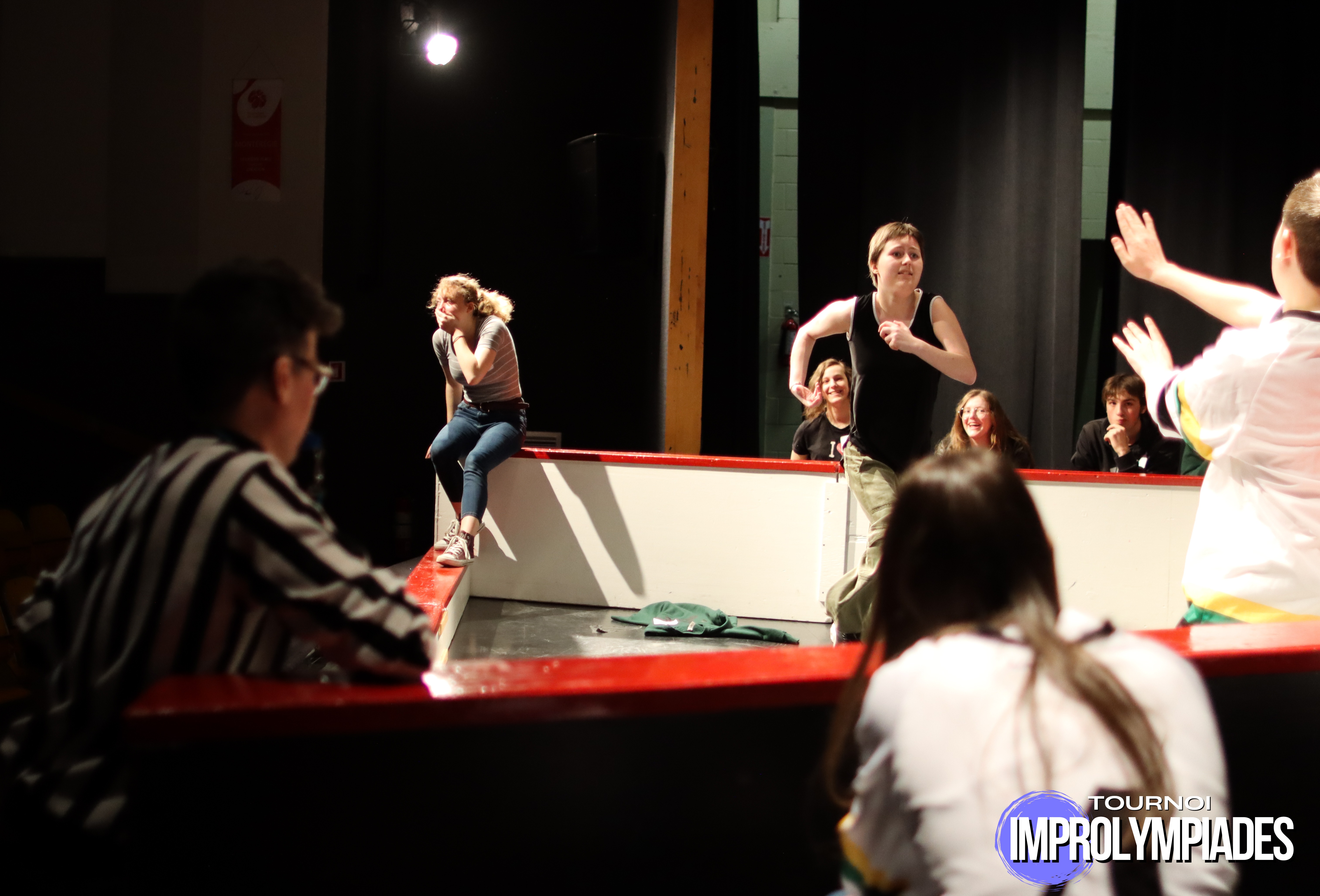 Participants en action dans une arène d’improvisation lors d’un match, avec arbitre et public visibles autour de la zone de jeu.