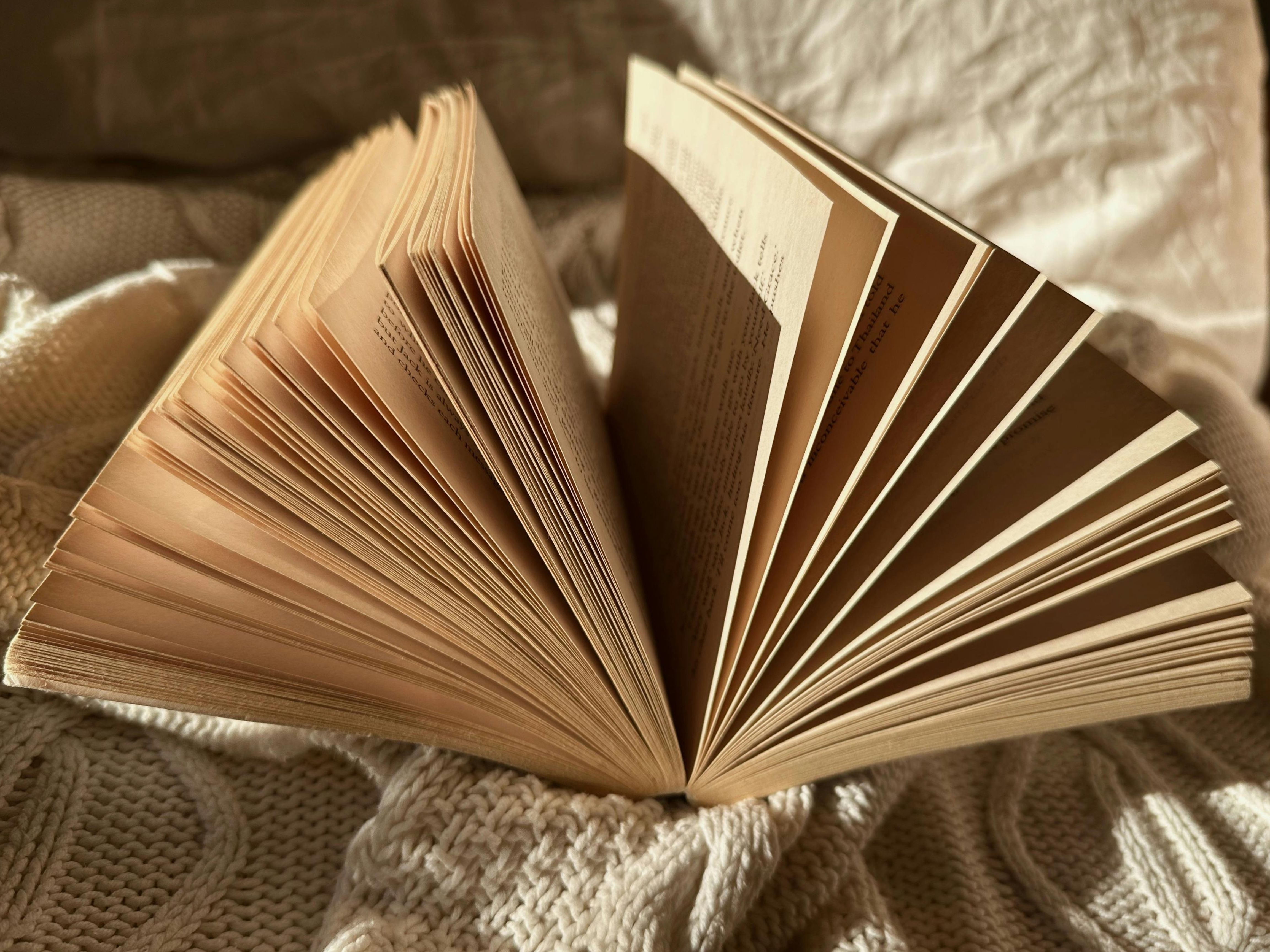 Livre ouvert posé sur un tissu texturé, avec ses pages déployées en éventail sous une lumière chaude, évoquant un atelier de reliure japonaise.