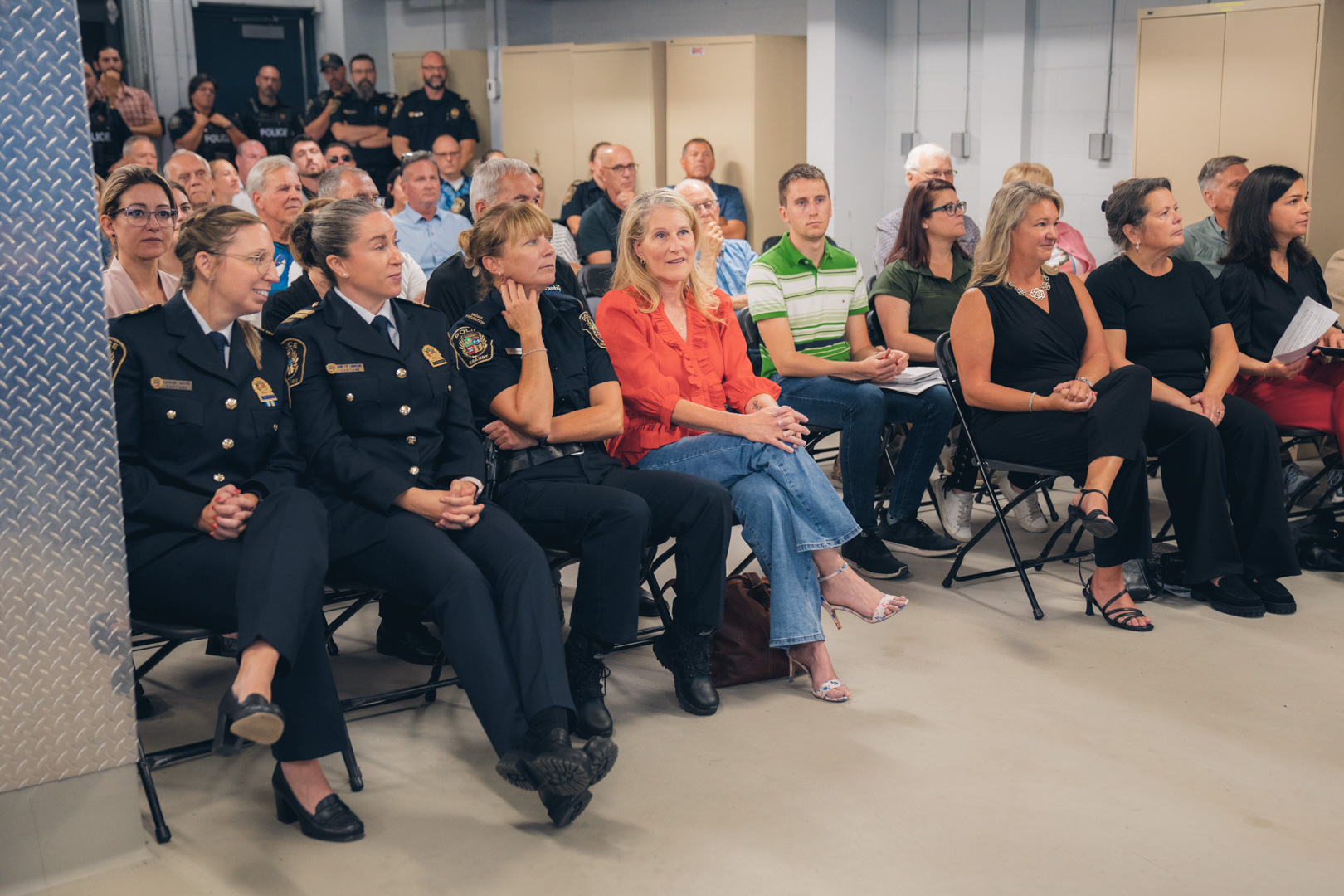 Public assis dans une salle, incluant des policiers en uniforme, lors d’une cérémonie officielle.