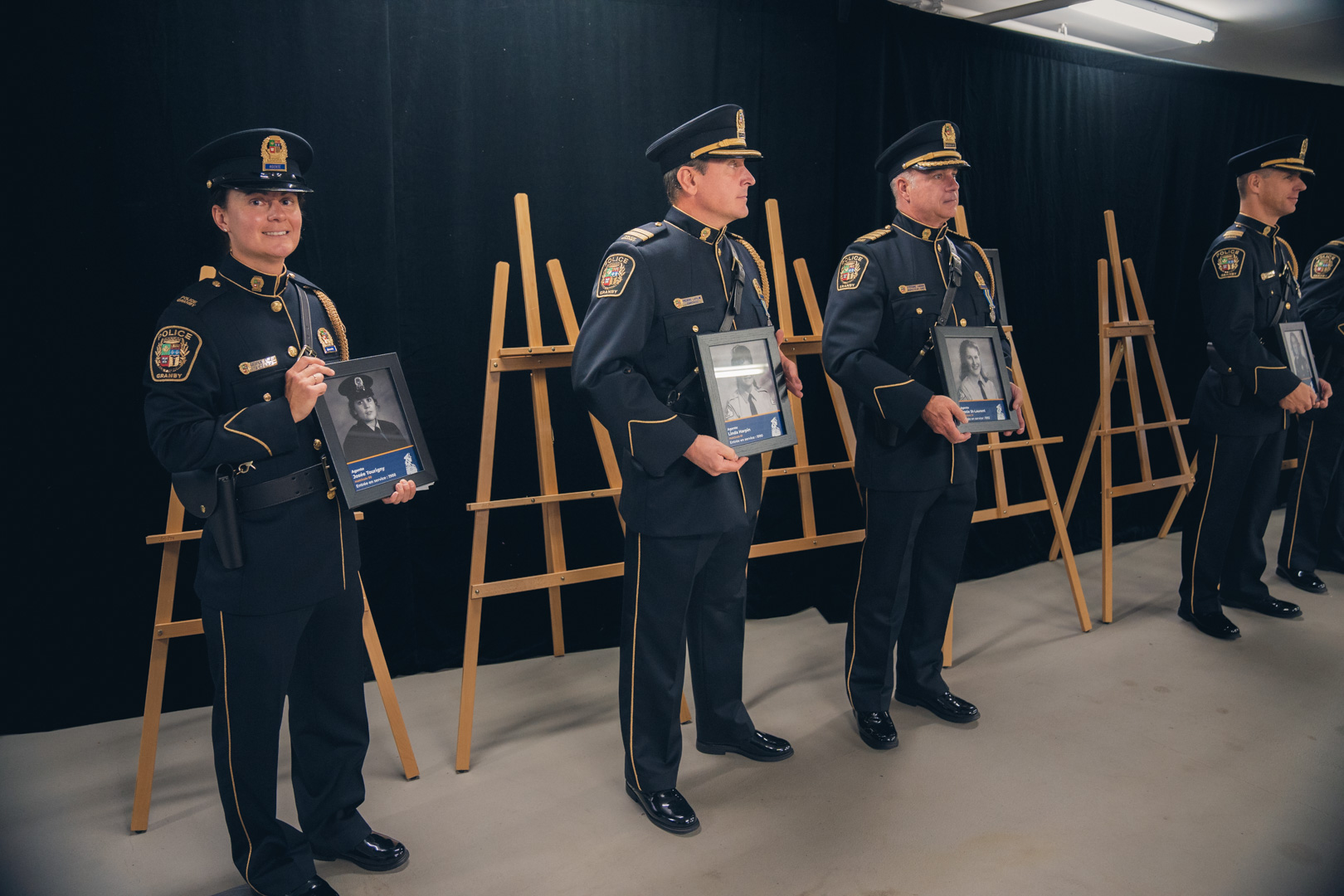  Policiers en uniforme alignés, tenant des cadres avec photos devant des chevalets. 