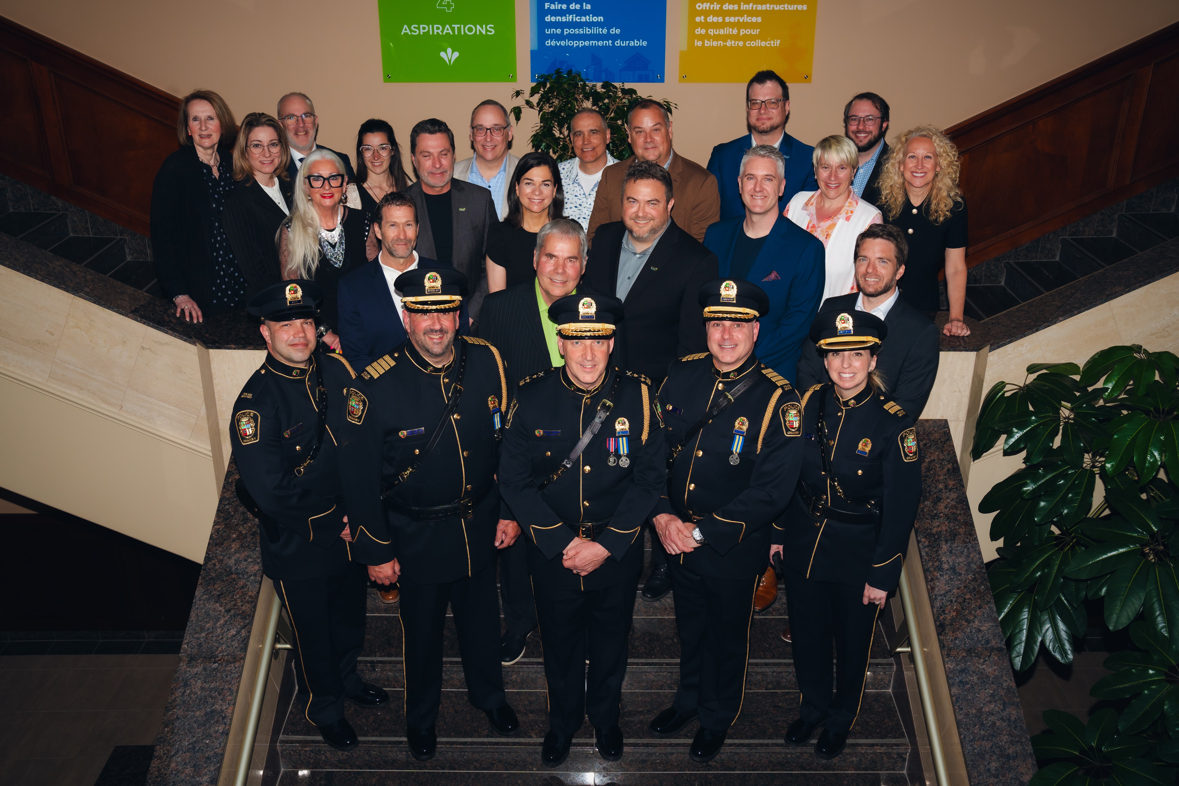 Photo de groupe prise sur un escalier intérieur, avec plusieurs agents en uniforme du Service de police de Granby au premier rang et des personnes en tenue civile derrière eux.
