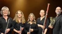 Groupe de cinq musiciens vêtus de noir tenant des instruments et éclairé par des projecteurs.